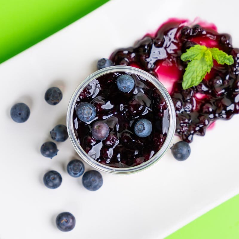 Top view of fresh blueberry jam with whole berries and mint on a white plate.