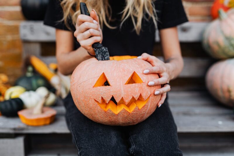 Woman carving a jack-o'-lantern on a bench, perfect for fall celebrations.