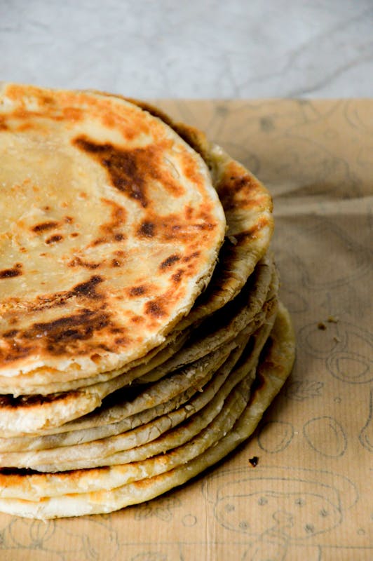 A stack of freshly baked homemade flatbread on rustic paper, showcasing a golden crispy texture.