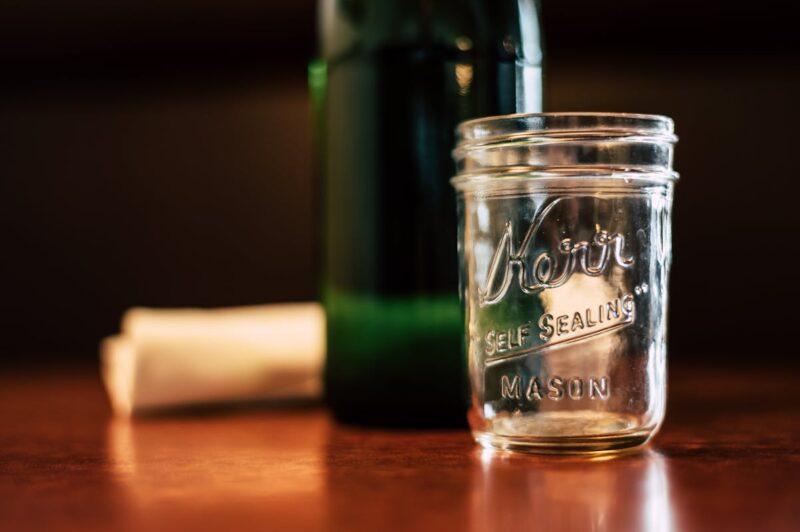 An empty Kerr mason jar placed on a wooden table indoors with soft background lighting.