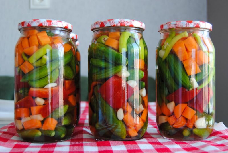 Three jars of assorted pickled vegetables on a red checkered tablecloth.