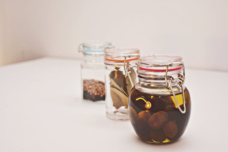 A still life photo featuring various preserved and pickled jars with olives and spices.